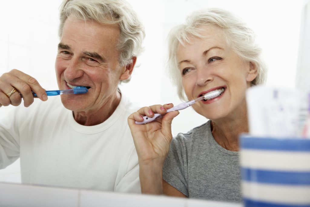 male and female seniors brushing teeth side by side